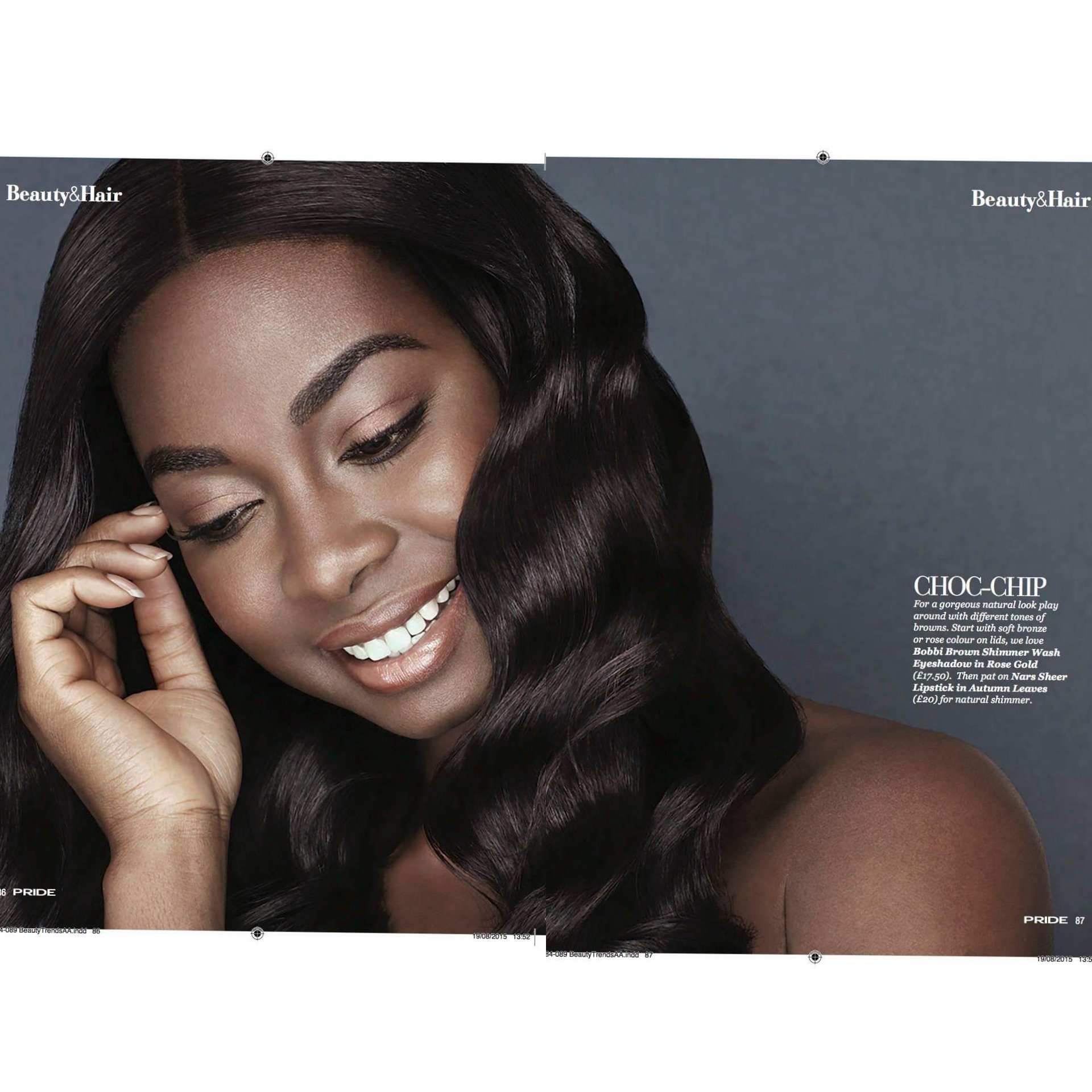 Close-up of a woman with long, wavy dark hair, smiling with closed eyes, and touching her face, in an advertisement for beauty and hair products.