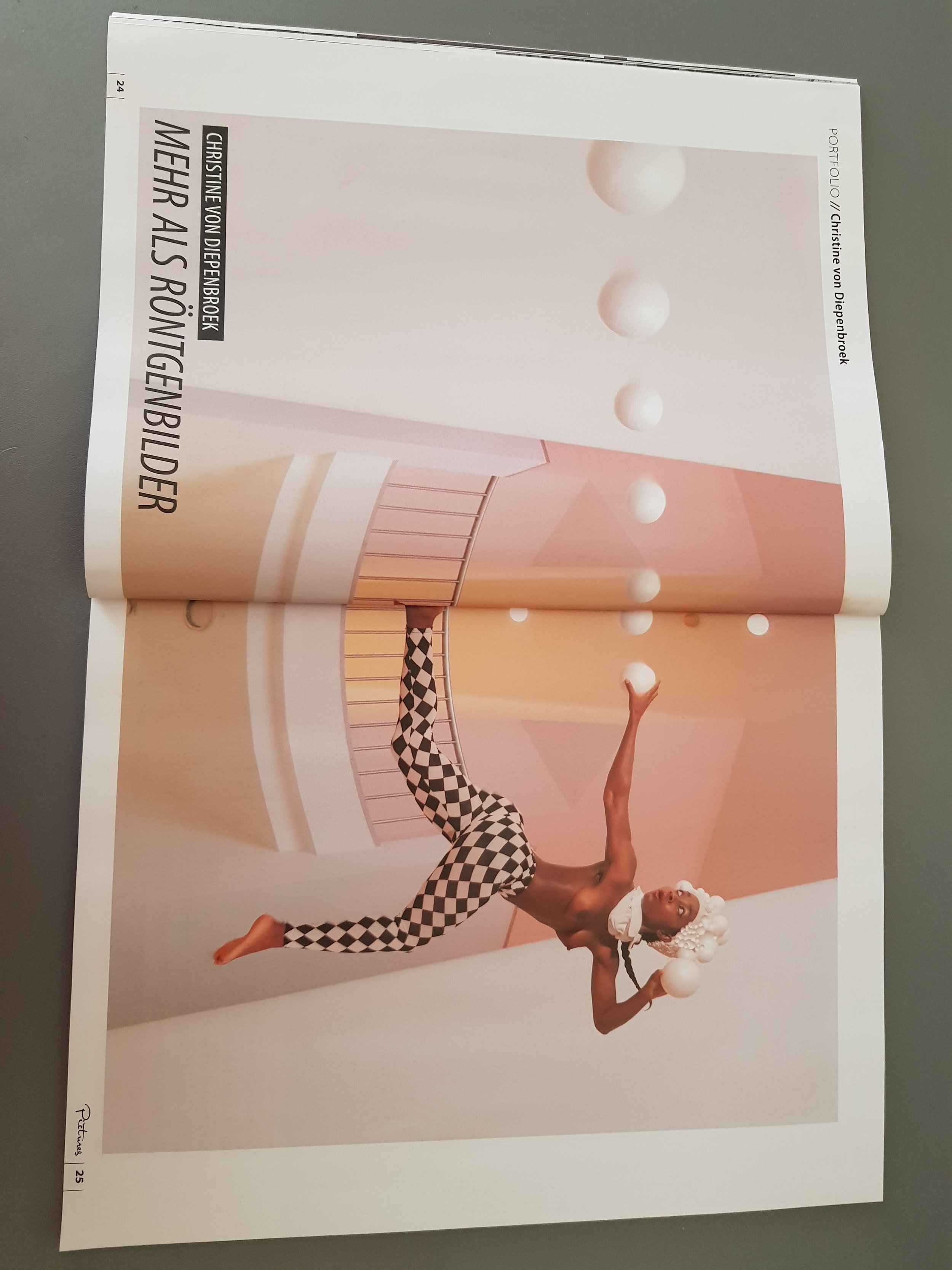 A magazine or photo spread showing a person dressed in checkered pants and a white wig performing a balancing act with white balls in a stylized, pastel-colored, geometric set.