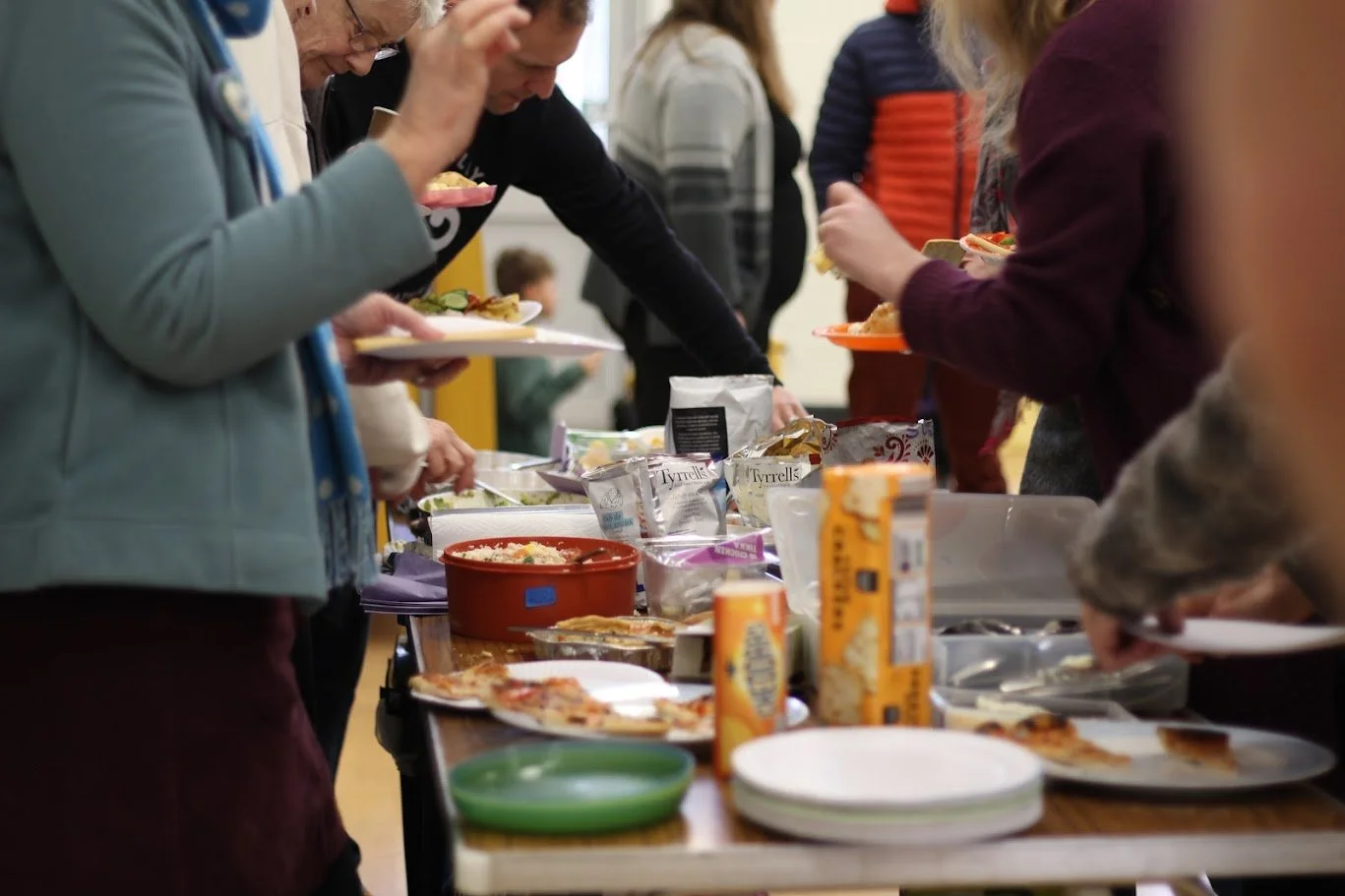 People gathered around a table serving themselves food at a buffet-style meal.