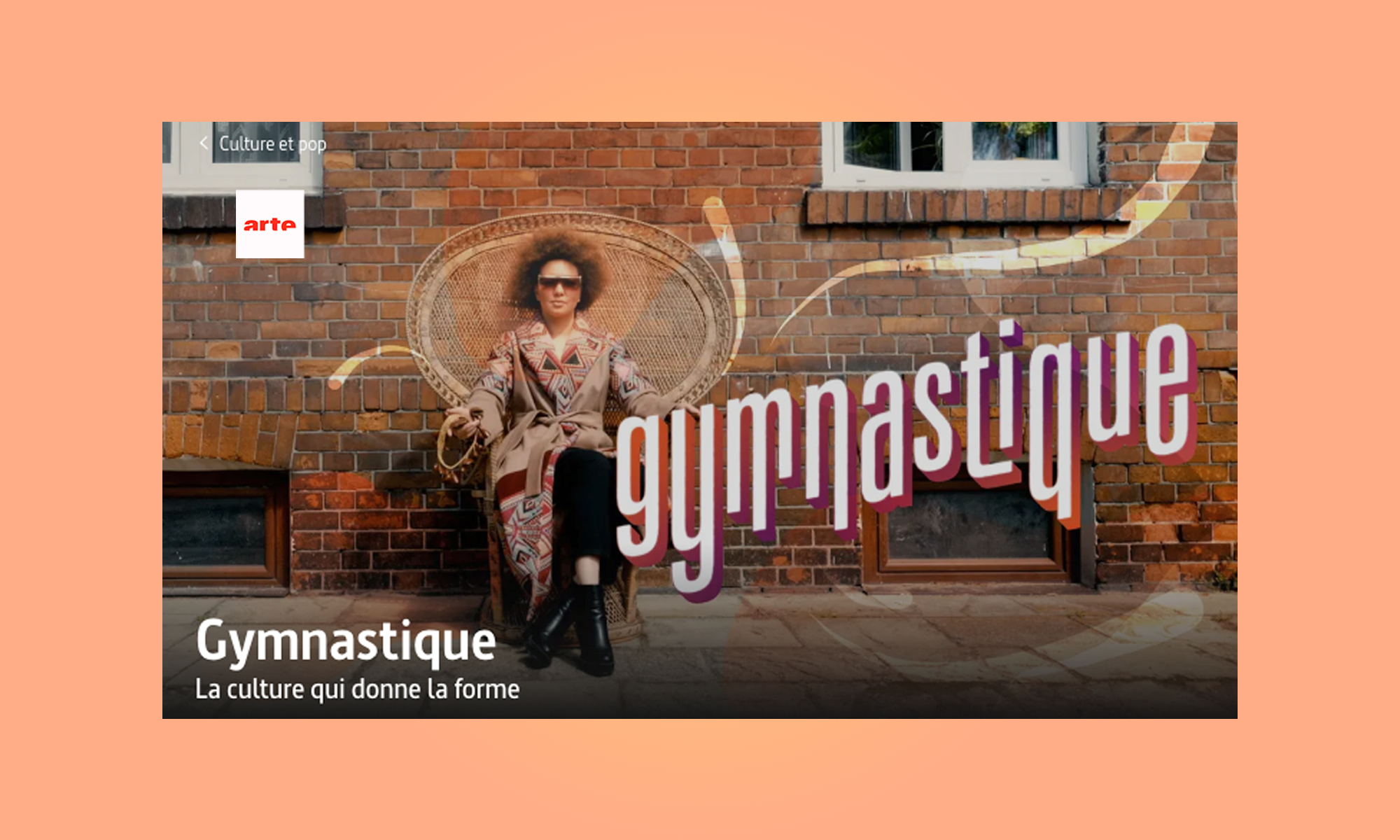 Personne assise sur un fauteuil en osier devant un mur de briques avec des textes « Gymnastique » et « La culture qui donne la forme ».