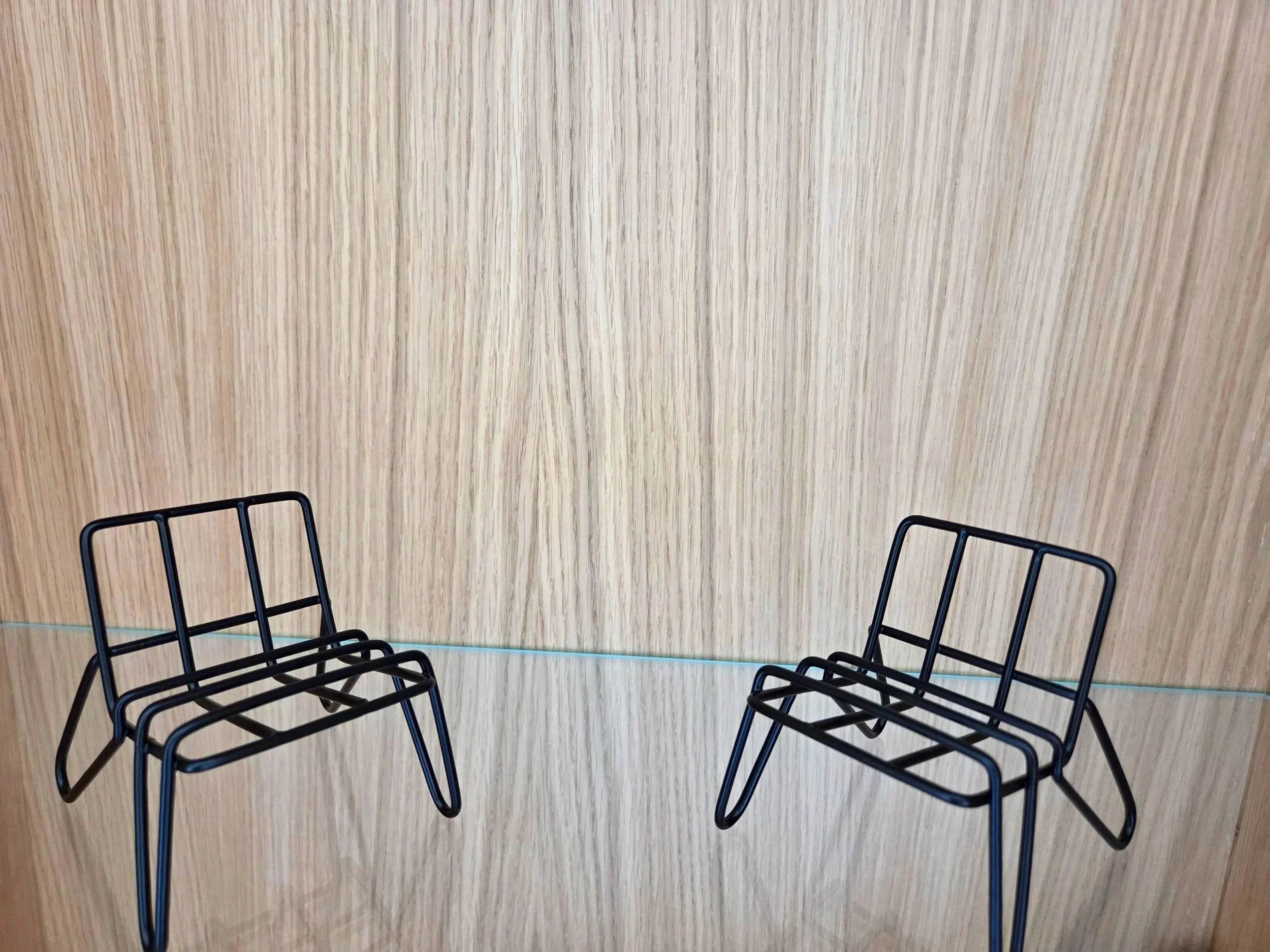 Zwei schwarze Metallstühle stehen gegenüber vor einer Holzwand.