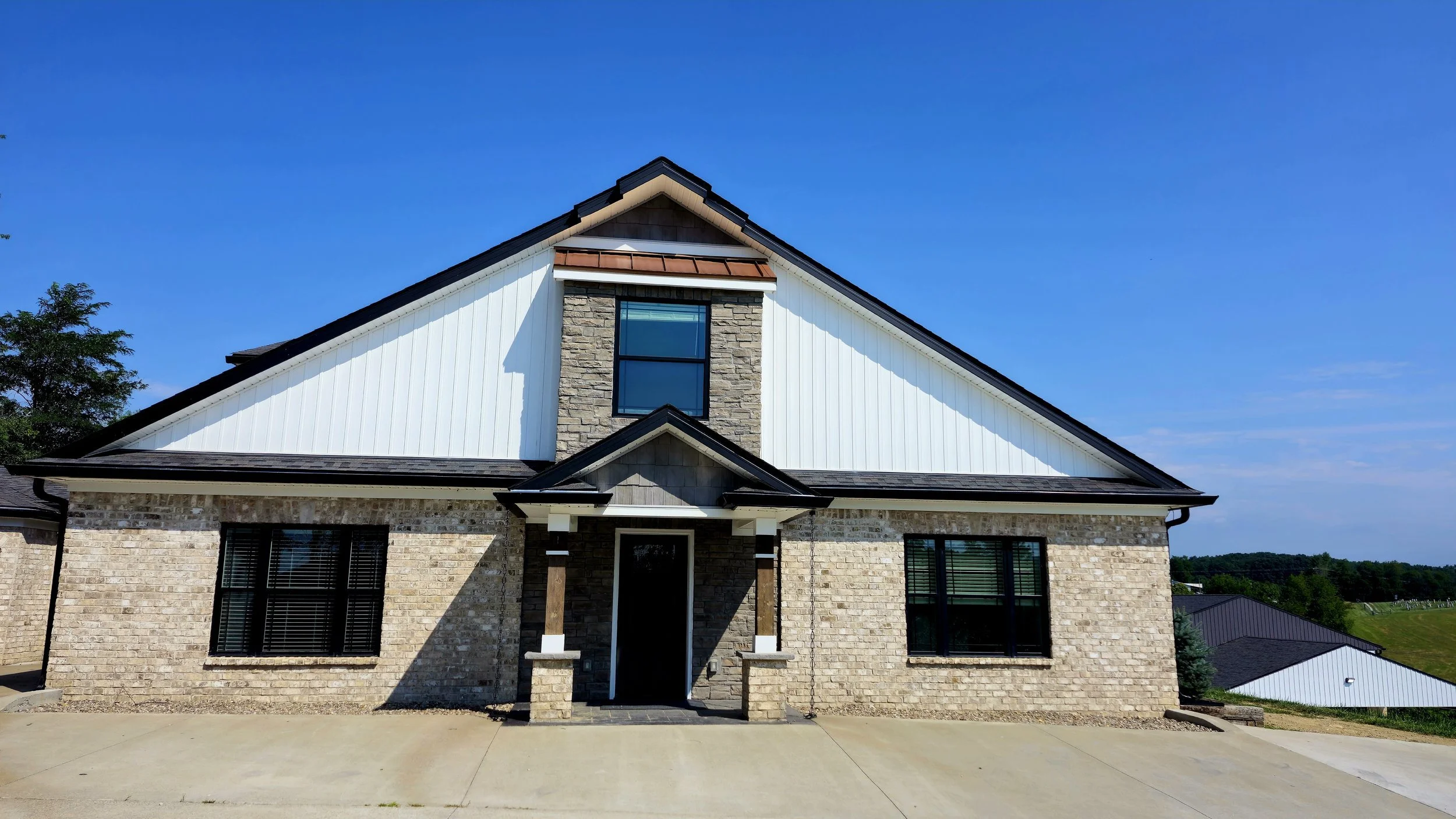 Front view of a modern house with brick and painted siding, gable roof, and large windows, under a blue sky.