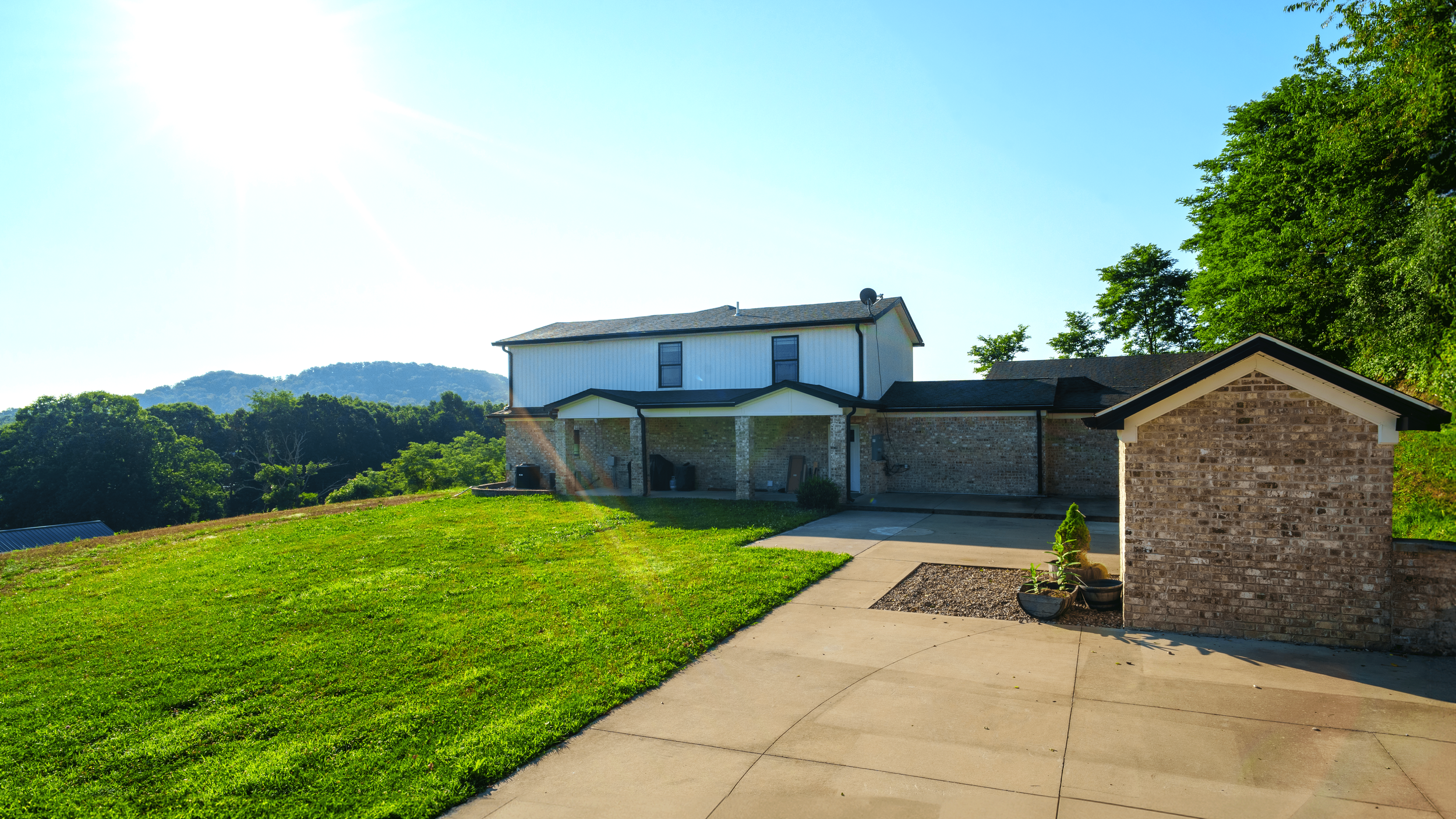 Backyard with a house, a brick shed, and green trees, under a clear blue sky with sunlight.
