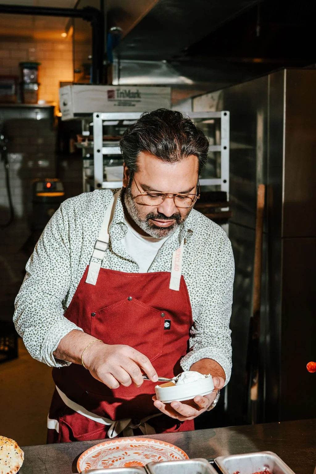 Man in glasses and a red apron preparing food in a kitchen.