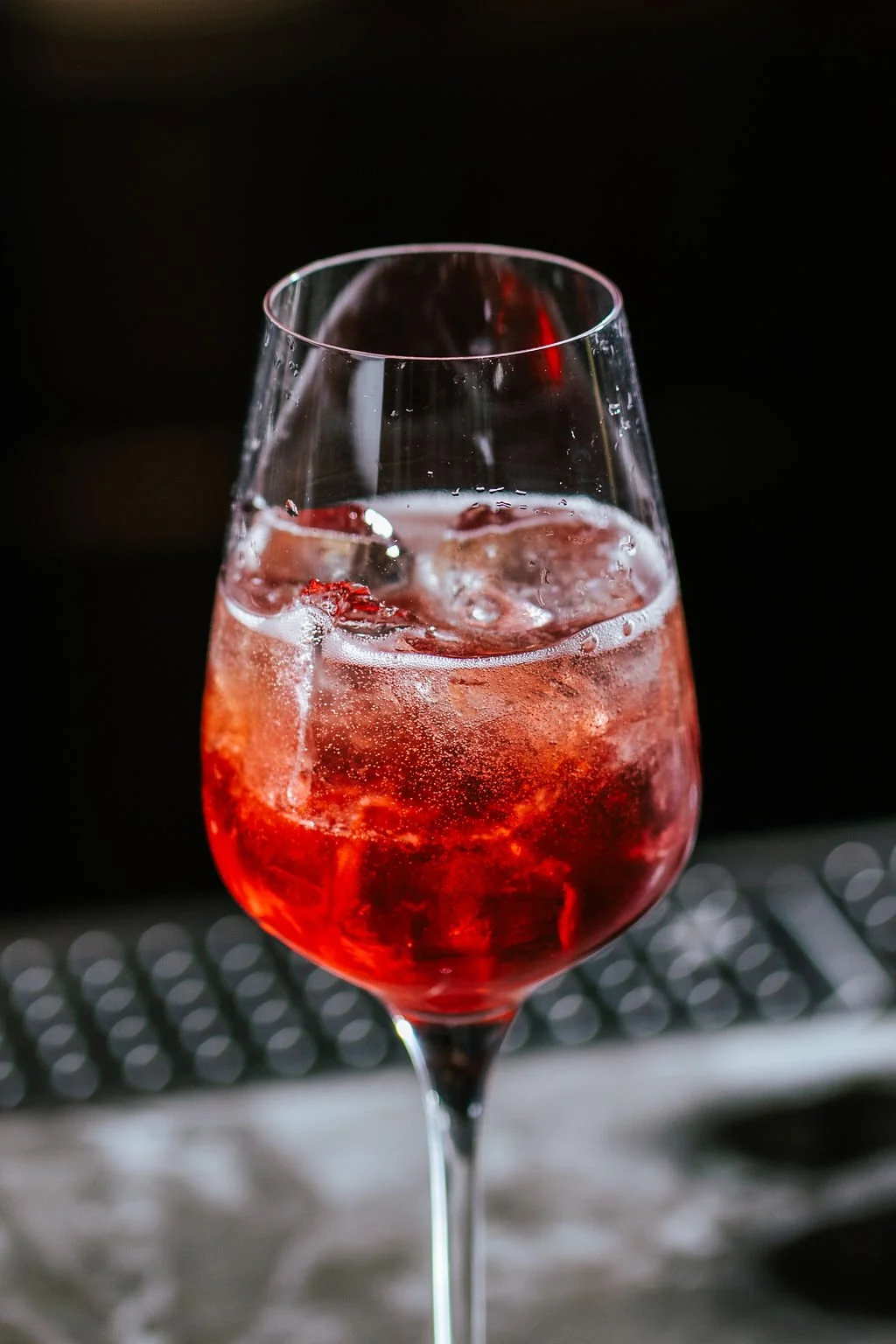 A glass of red wine with ice cubes against a dark background.