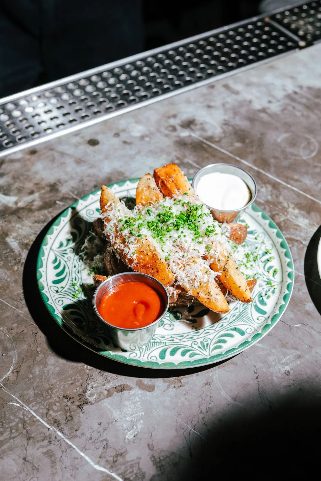 Plate of nachos topped with grated cheese, chopped herbs, and fried potato wedges, served with sides of salsa and sour cream.