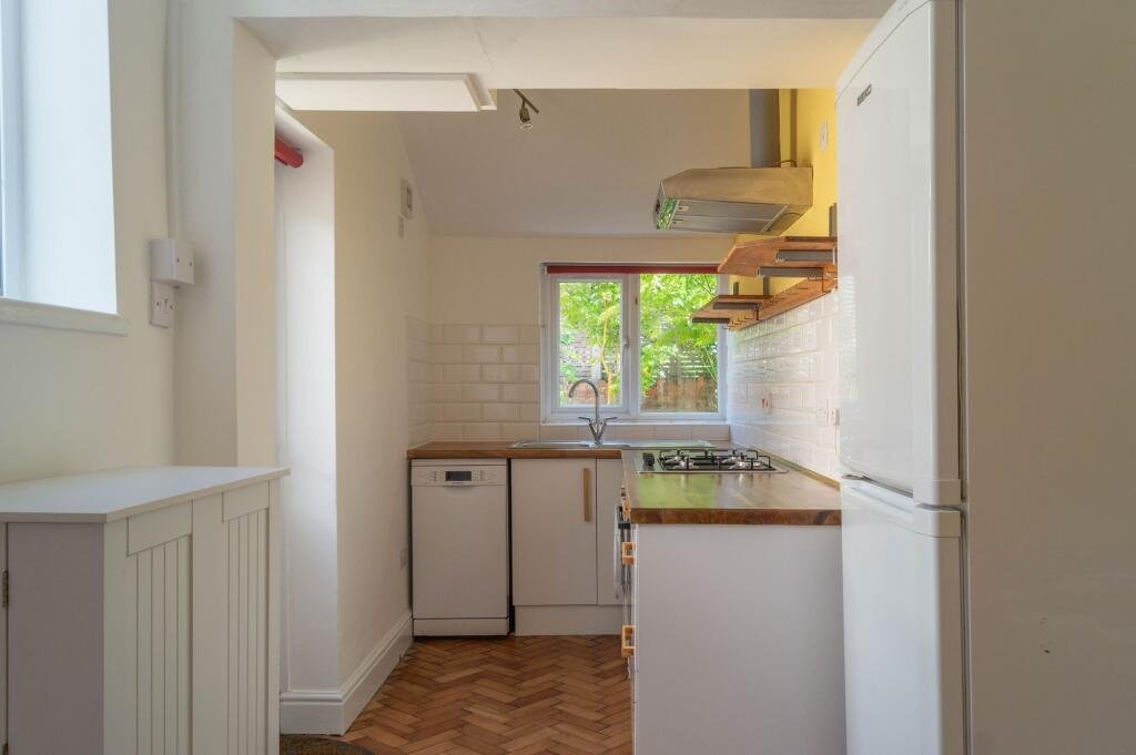 Small kitchen with white appliances, a window overlooking greenery, and wooden shelves.