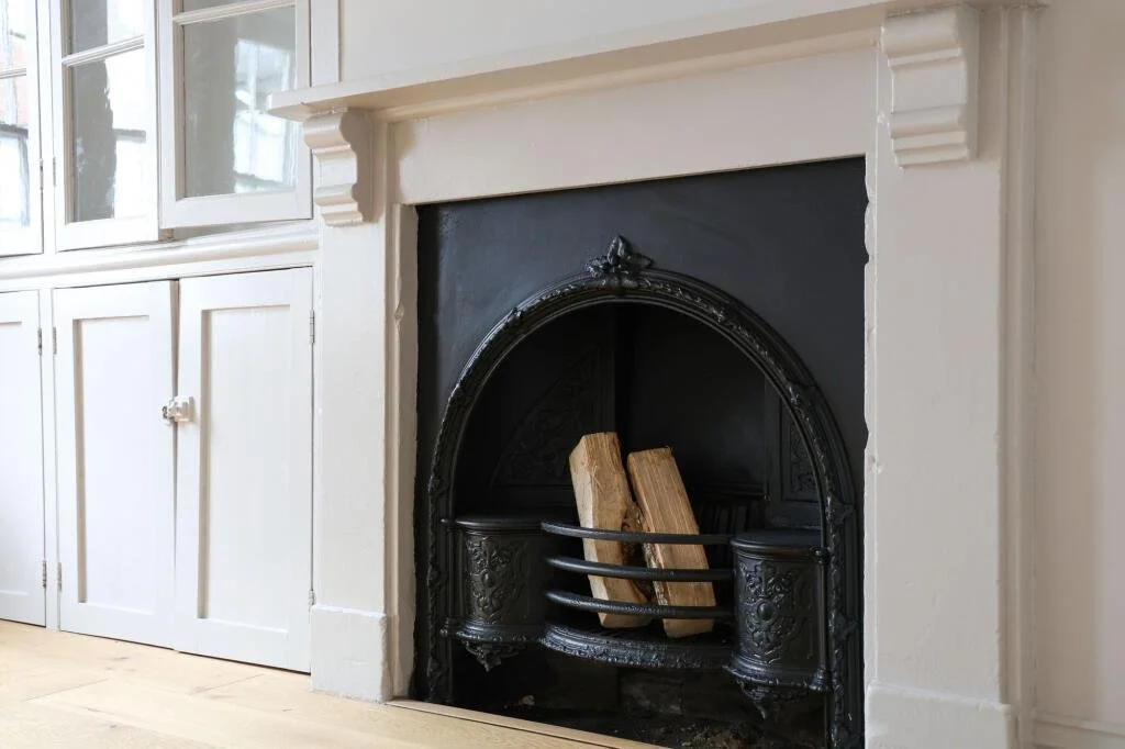 A fireplace with a black cast iron insert and wood logs inside, surrounded by a white mantel and built-in white cabinets.