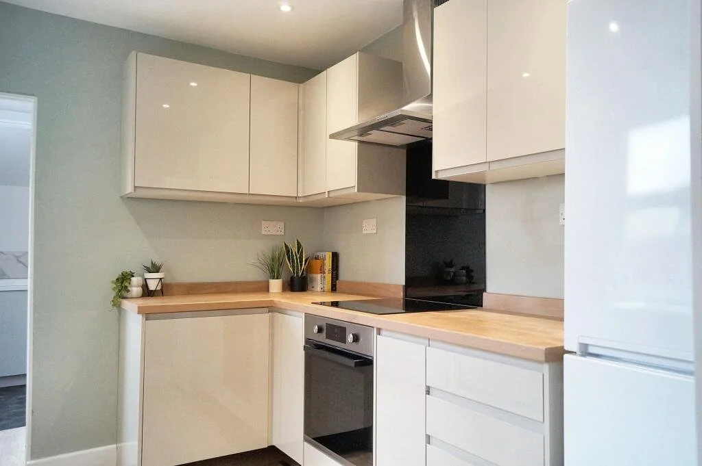 Modern kitchen with white cabinetry, wooden countertops, and a stainless steel range hood.