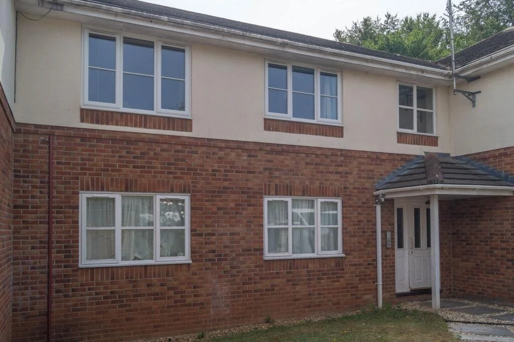 The exterior of a two-story residential building with brick and stucco walls, white-framed windows, and a small entrance porch with a white door and a tiled roof.