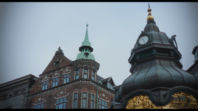 A close-up view of ornate buildings with detailed architectural elements, including a gold-decorated clock and spires under an overcast sky.png