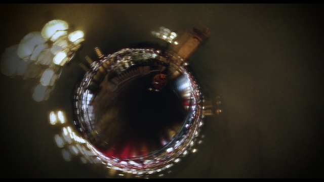 An abstract, aerial-like view of a cityscape at night, distorted through a circular, fisheye effect that wraps the scene into a spherical form, centered around glowing city lights.