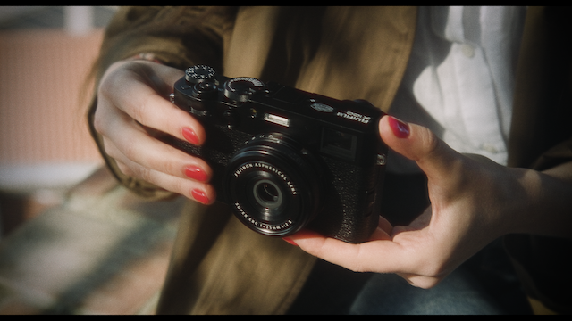 A woman holds a vintage camera in her hands, slightly cradling it as sunlight gently illuminates her and the camera.png