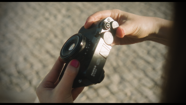 A woman smiles gently while looking down at her camera, with the light softening her features and highlighting her serene expression.png