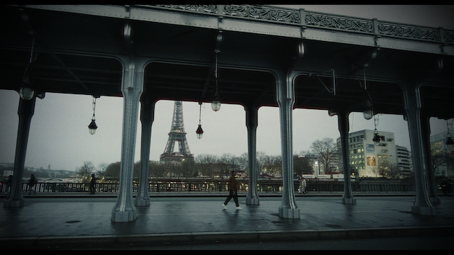 Another symmetrical shot under a bridge featuring classical architectural details with a view of the Eiffel Tower in the distance, evoking a serene, almost melancholic ambiance.