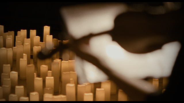 An abstract, artistic shot focusing on a blurred violin bow with a backdrop of many unlit candles, creating a soft, glowing effect.