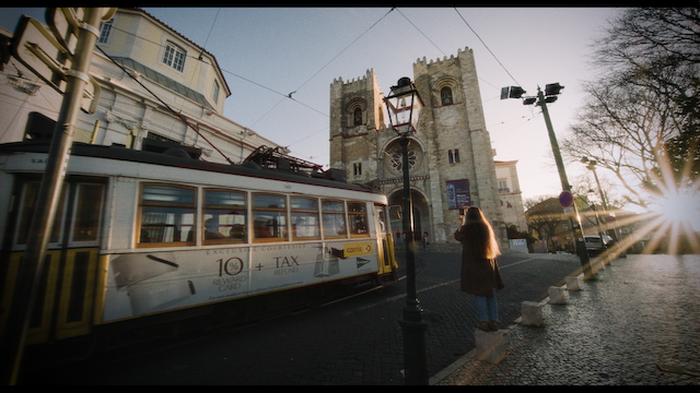 A woman observes a passing tram near a historic cathedral in a sunlit square.