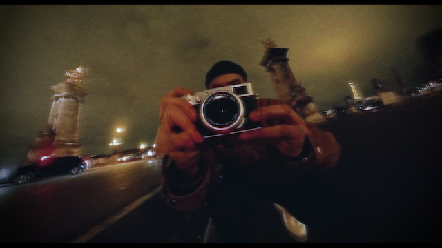 Night shot of a photographer holding up a camera to take a photo, with historic city monuments illuminated in the background, creating a mysterious and dramatic nighttime atmosphere.