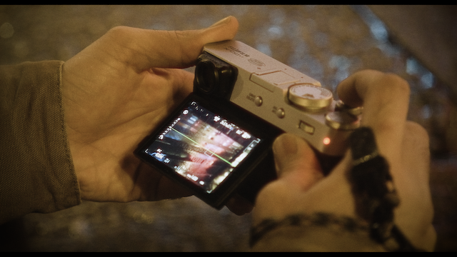 An image of a digital camera held by a pair of hands, the LCD screen displaying a vivid, colorful night scene, highlighting the modern photographic technology in a dark setting.