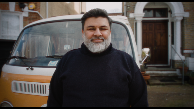 A man smiling broadly in front of his beloved vintage Volkswagen van.png