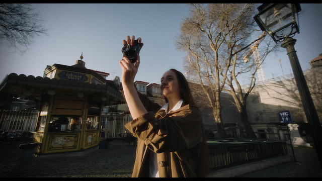 A woman takes a photo with her camera in a vibrant city park with a carousel in the background.png