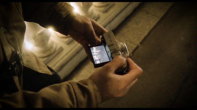 A person adjusting a digital camera's settings at night, the screen illuminated, showing another perspective of capturing moments amidst urban lighting.