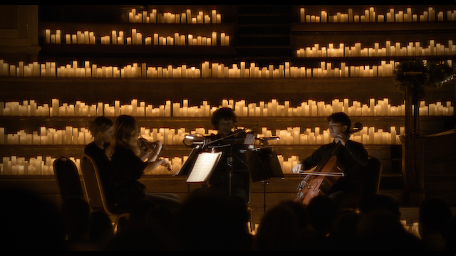 A quartet of string musicians performing in front of a large candle-lit backdrop, enveloped in a serene, warm ambiance that highlights the intimacy of the setting
