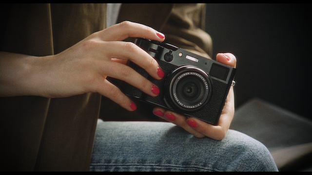Close-up of a woman's hands holding a black camera, with a coffee cup and saucer on a table nearby.