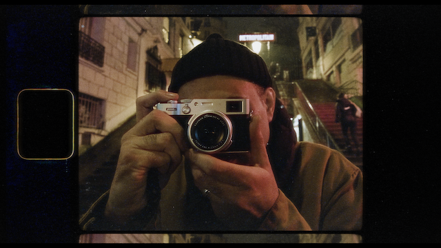 A reflective self-portrait of a photographer using a vintage camera, captured in a street mirror, adding layers of depth to the concept of observation and image capturing in an urban environment.