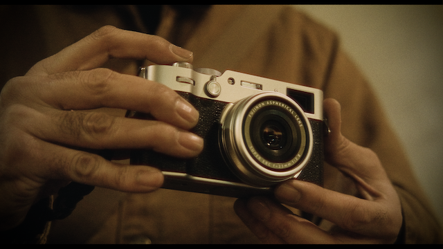 A detailed view of hands holding a retro-style camera, focusing on the tactile interaction between the photographer and his tool in a softly lit environment.