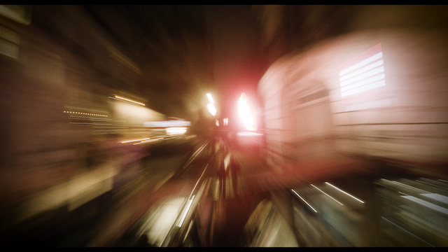 A dynamic, blurred street scene captured at night, conveying the motion and lights of the city in a streak of red and white, giving a sense of speed and urban energy.