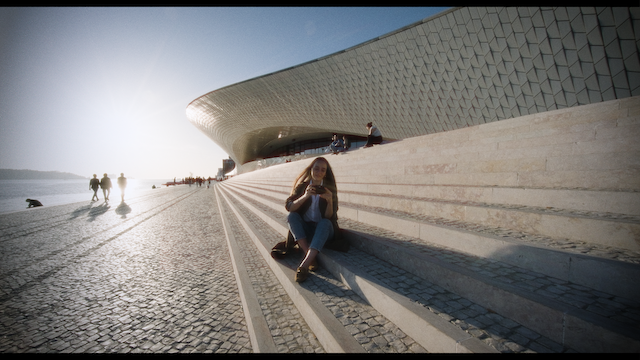 A woman sits on the steps of a contemporary building, capturing the vast architectural landscape in front of her.png