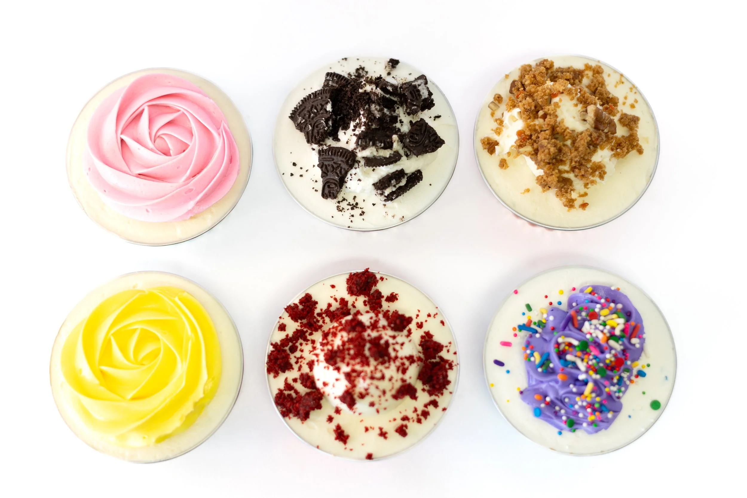 Six cupcakes with different colored frosting and toppings, arranged in two rows on a white background.