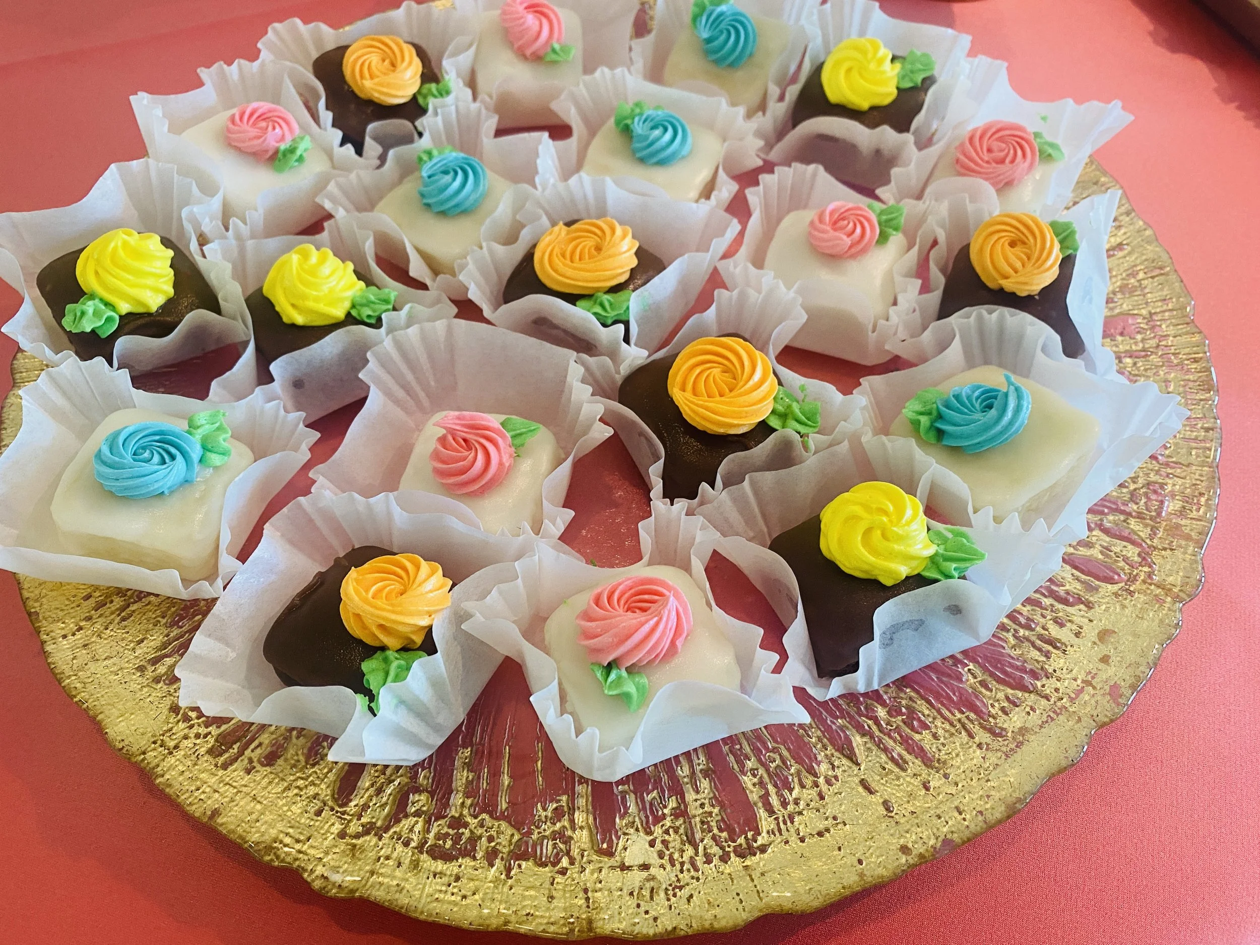 Assorted decorated petit fours with colorful frosting flowers on a gold serving tray.