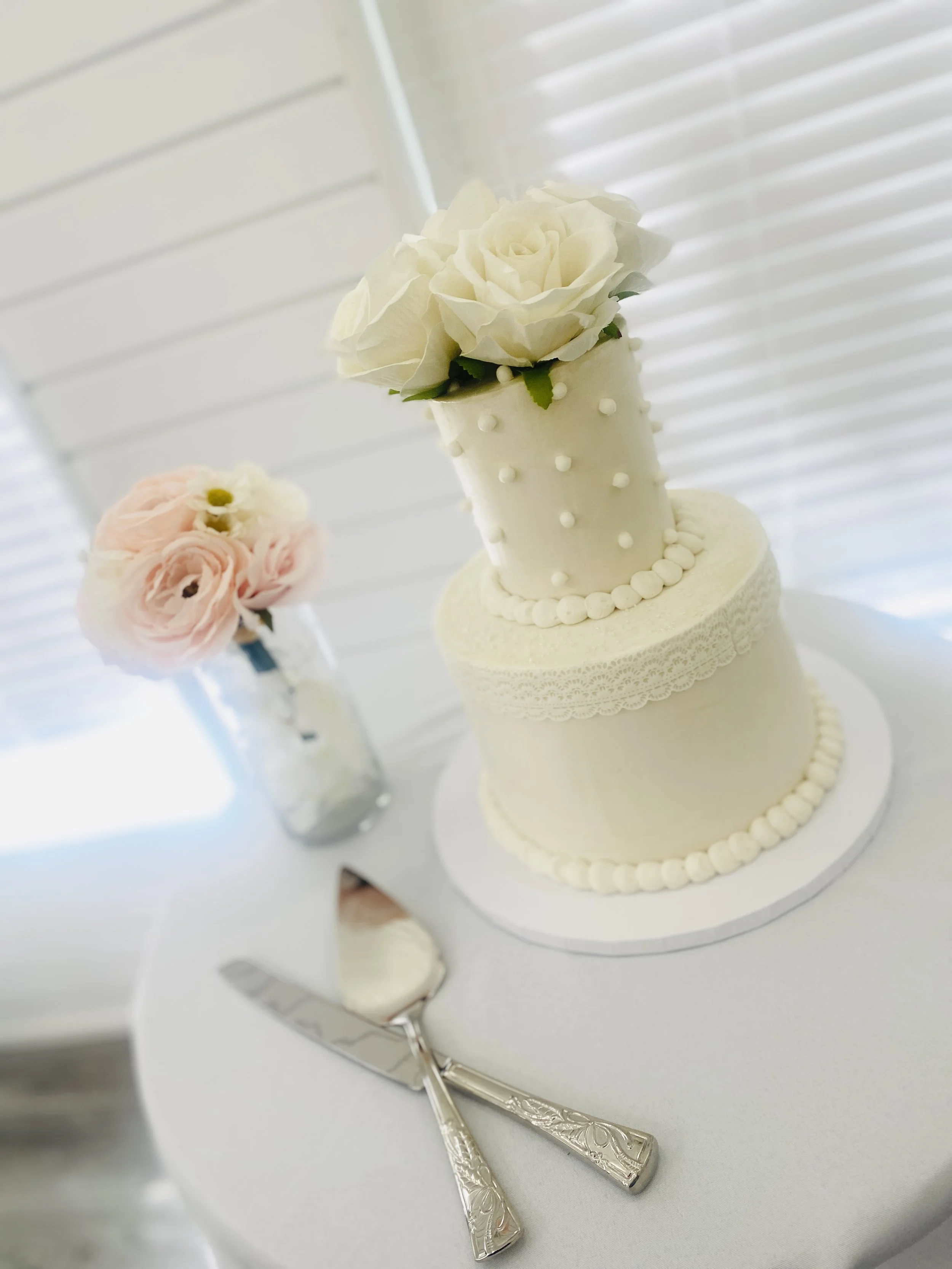 Elegant white wedding cake with floral decorations and a cake knife and server on a white table.