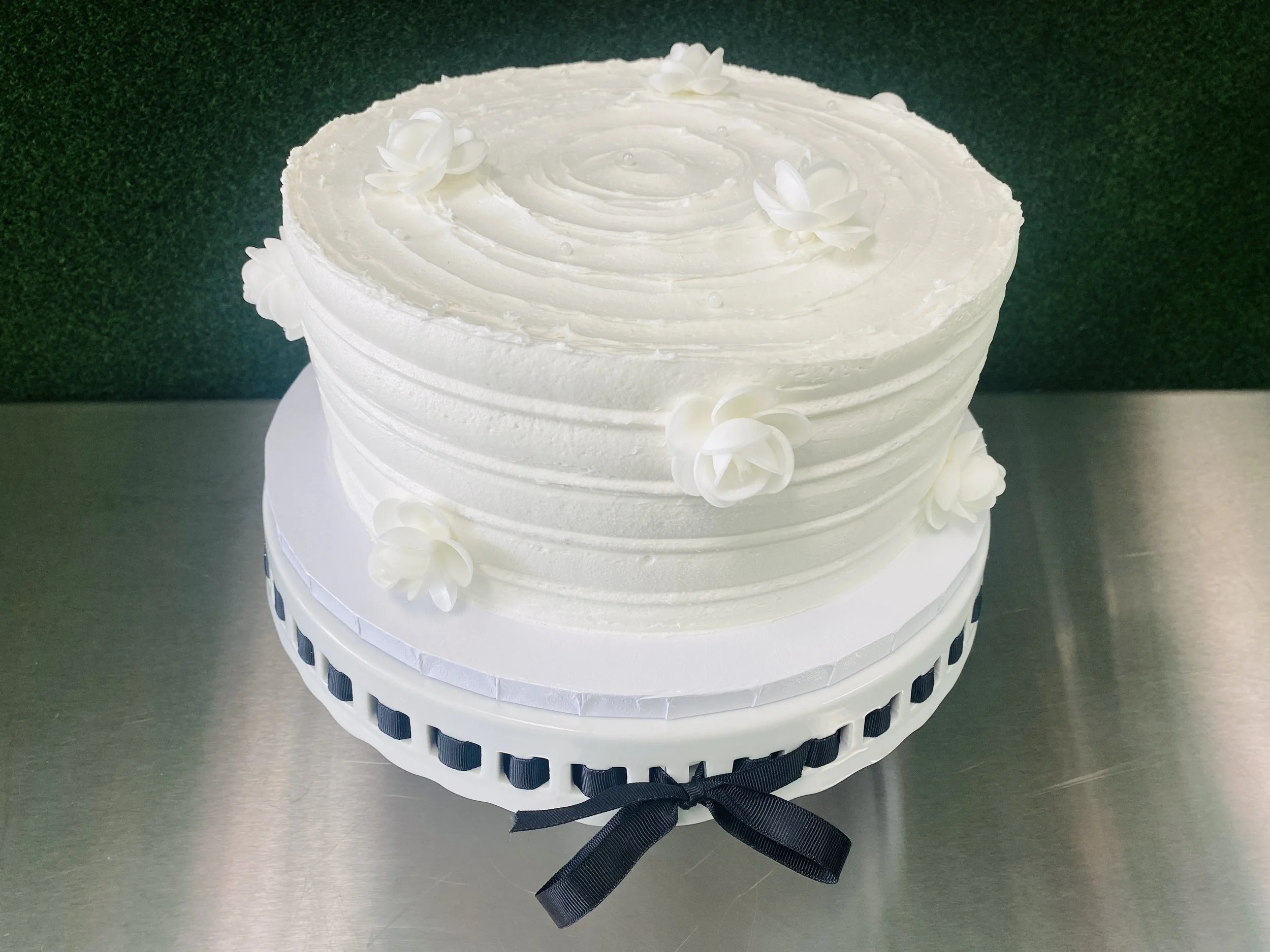 White tiered cake decorated with white flowers and a black ribbon around the base.