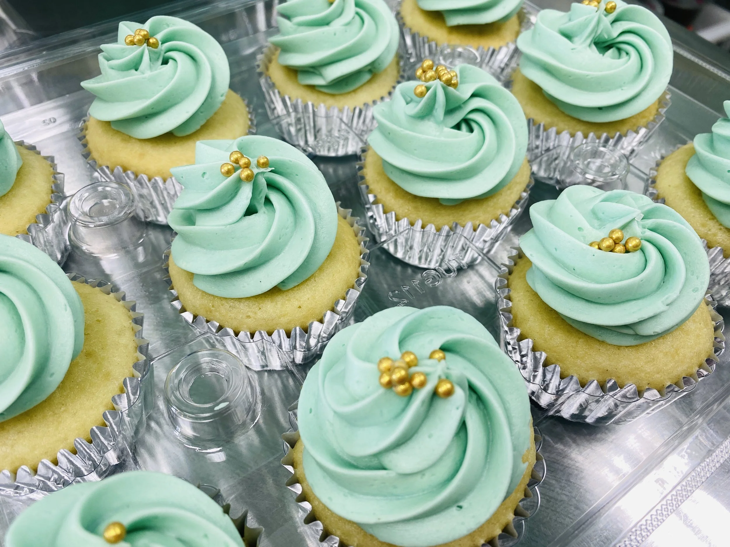 A tray of cupcakes with green frosting swirls topped with small gold edible beads.