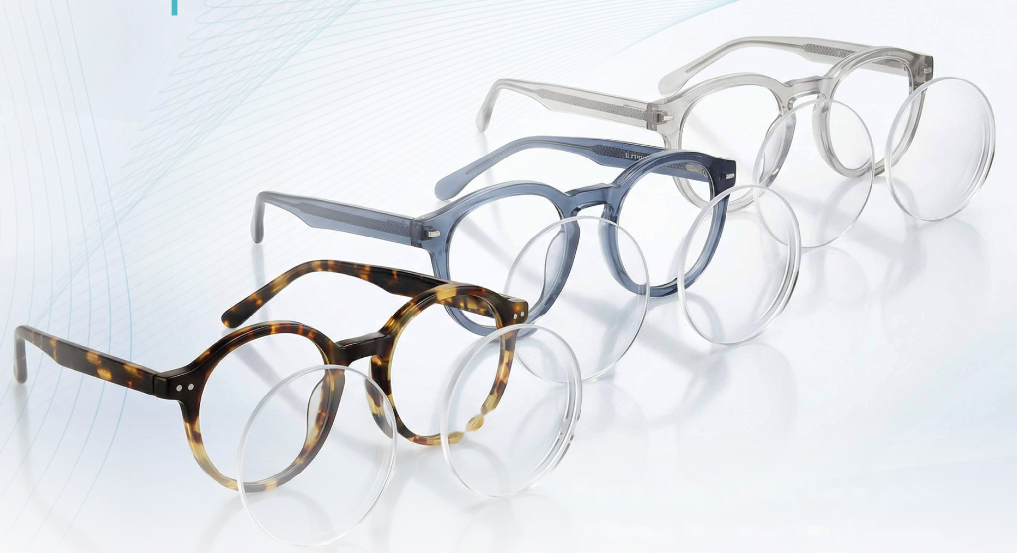 Four pairs of eyeglasses arranged on a pastel green surface with a fashion magazine, green leaves, and a person holding leafy branches on the magazine cover.