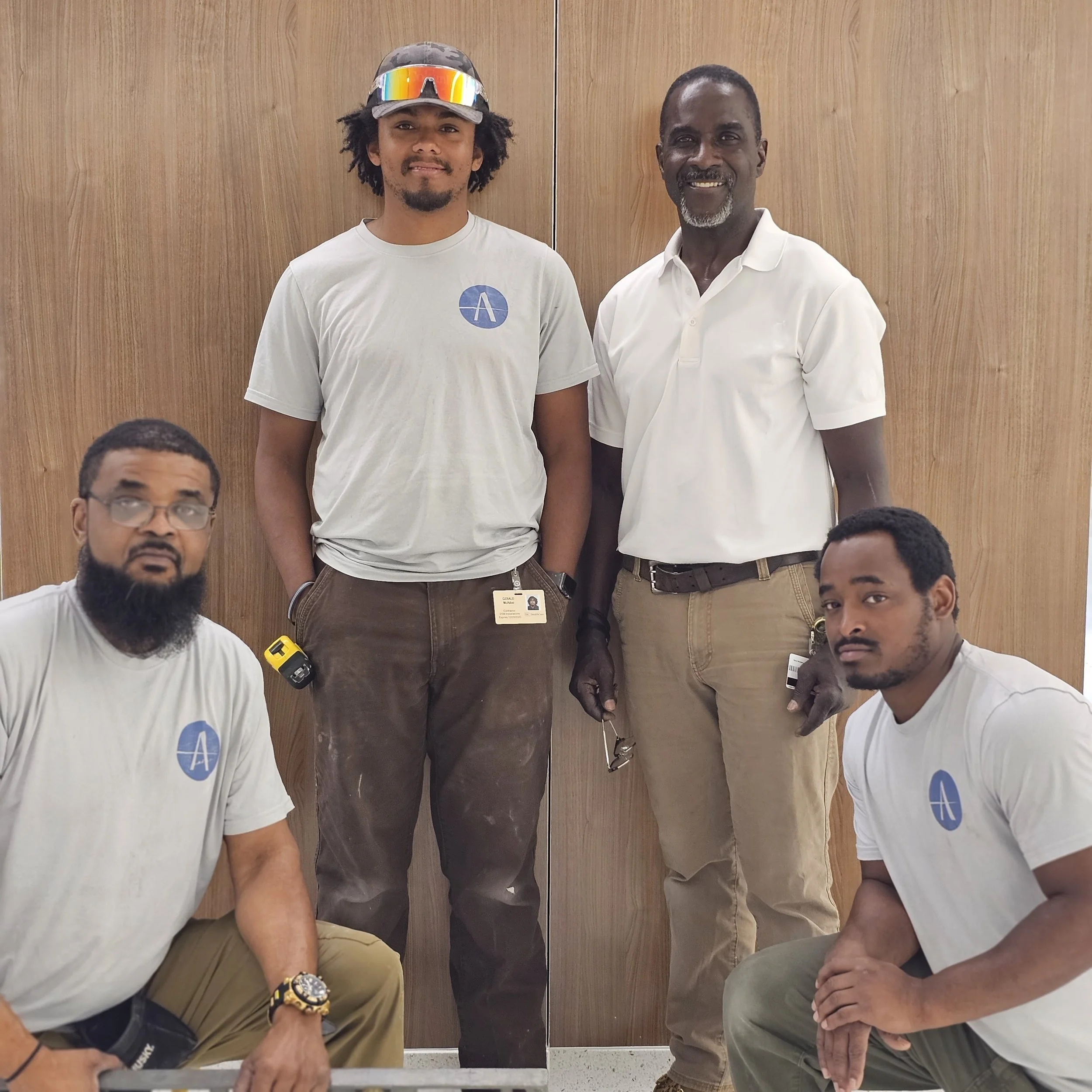 Four men posing in front of a wooden wall.