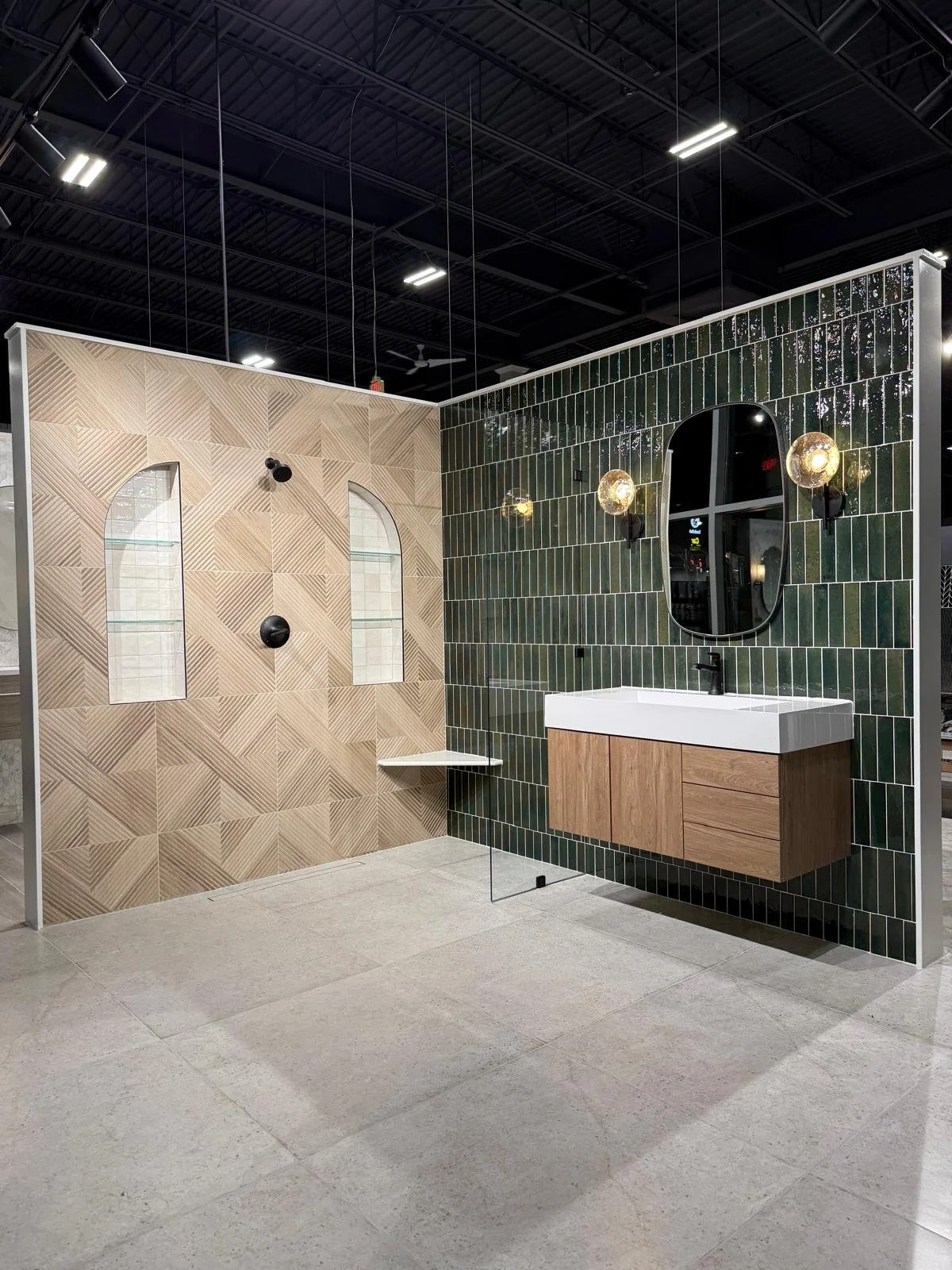Modern bathroom display with a green tiled wall, black mirror, wooden vanity, and lighting fixtures.