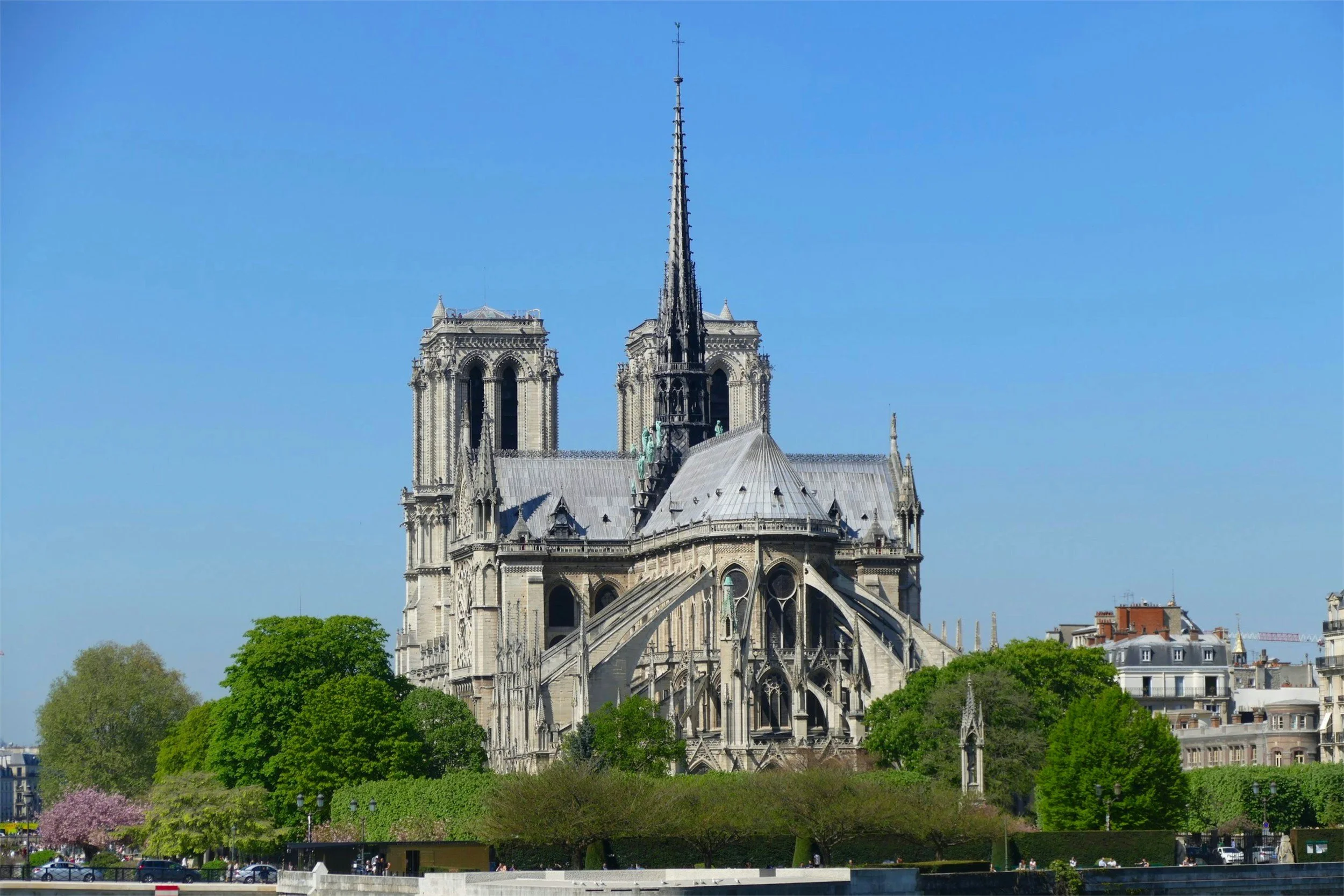 Notre Dame Cathedral in Paris with clear blue sky and green trees in the foreground.