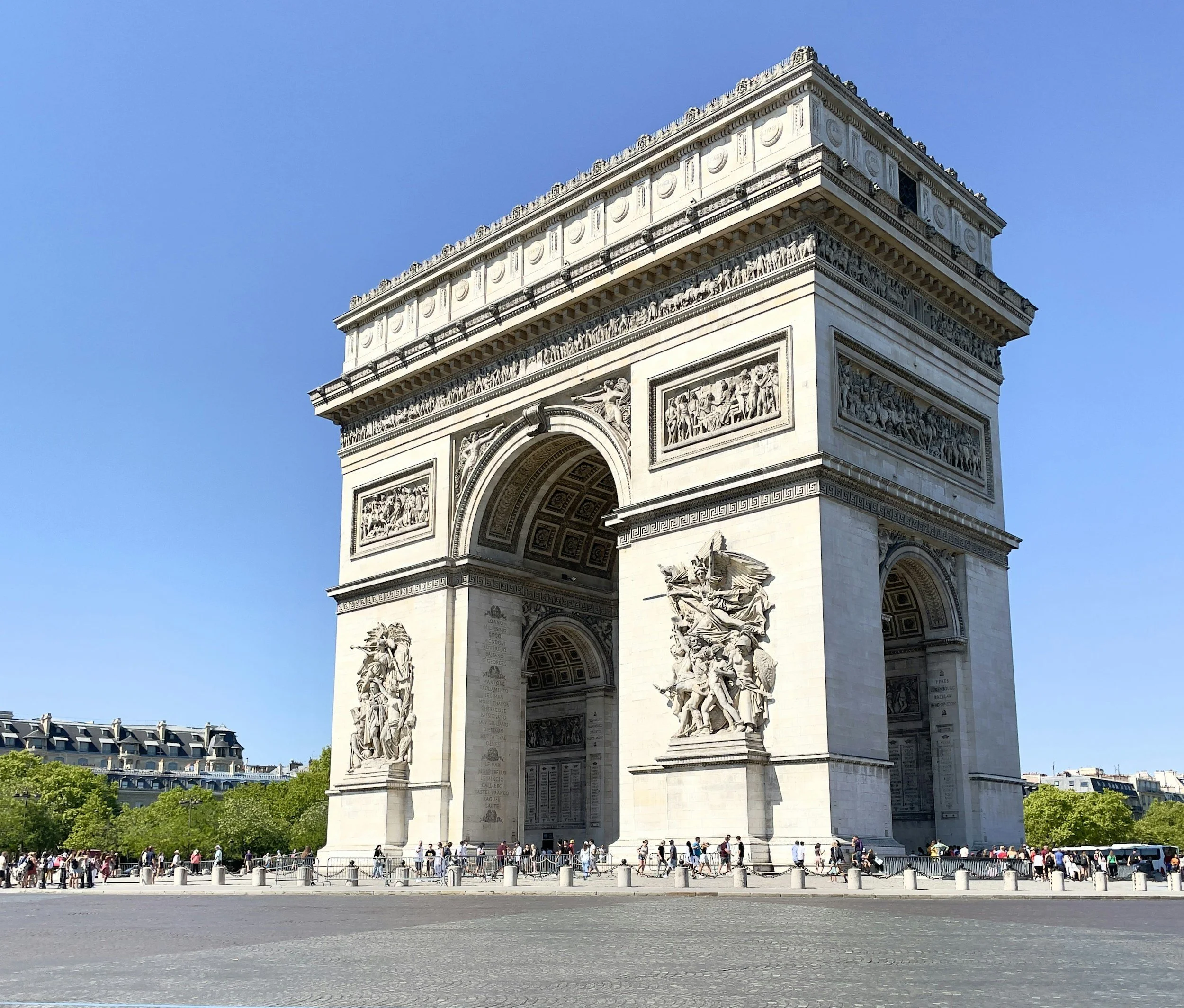 The Arc de Triomphe in Paris, France, with tourists walking around the monument on a clear, sunny day.