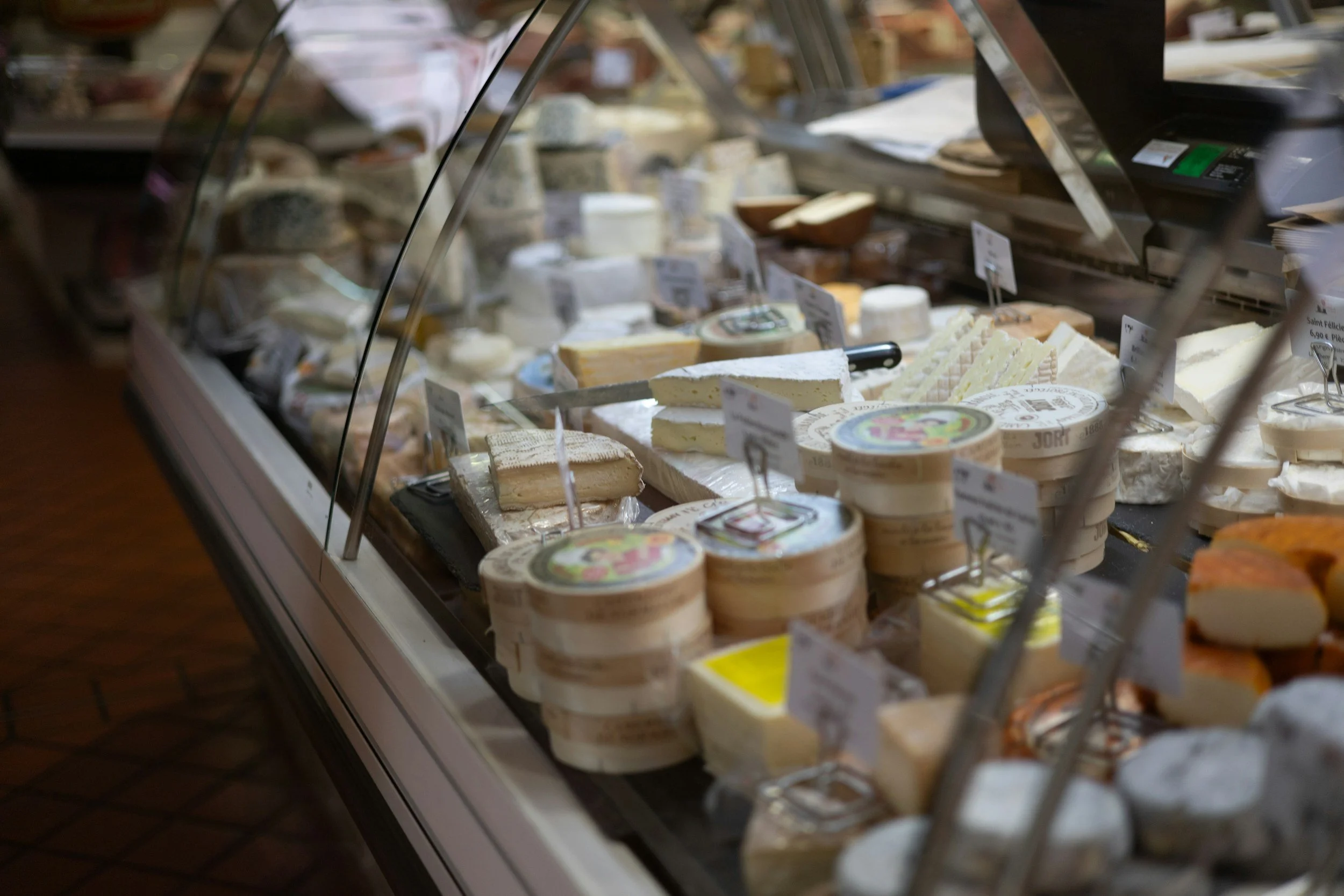 Display case filled with various cheeses, including soft cheeses, wedges, and pre-packaged cheese containers in a dairy or cheese shop.