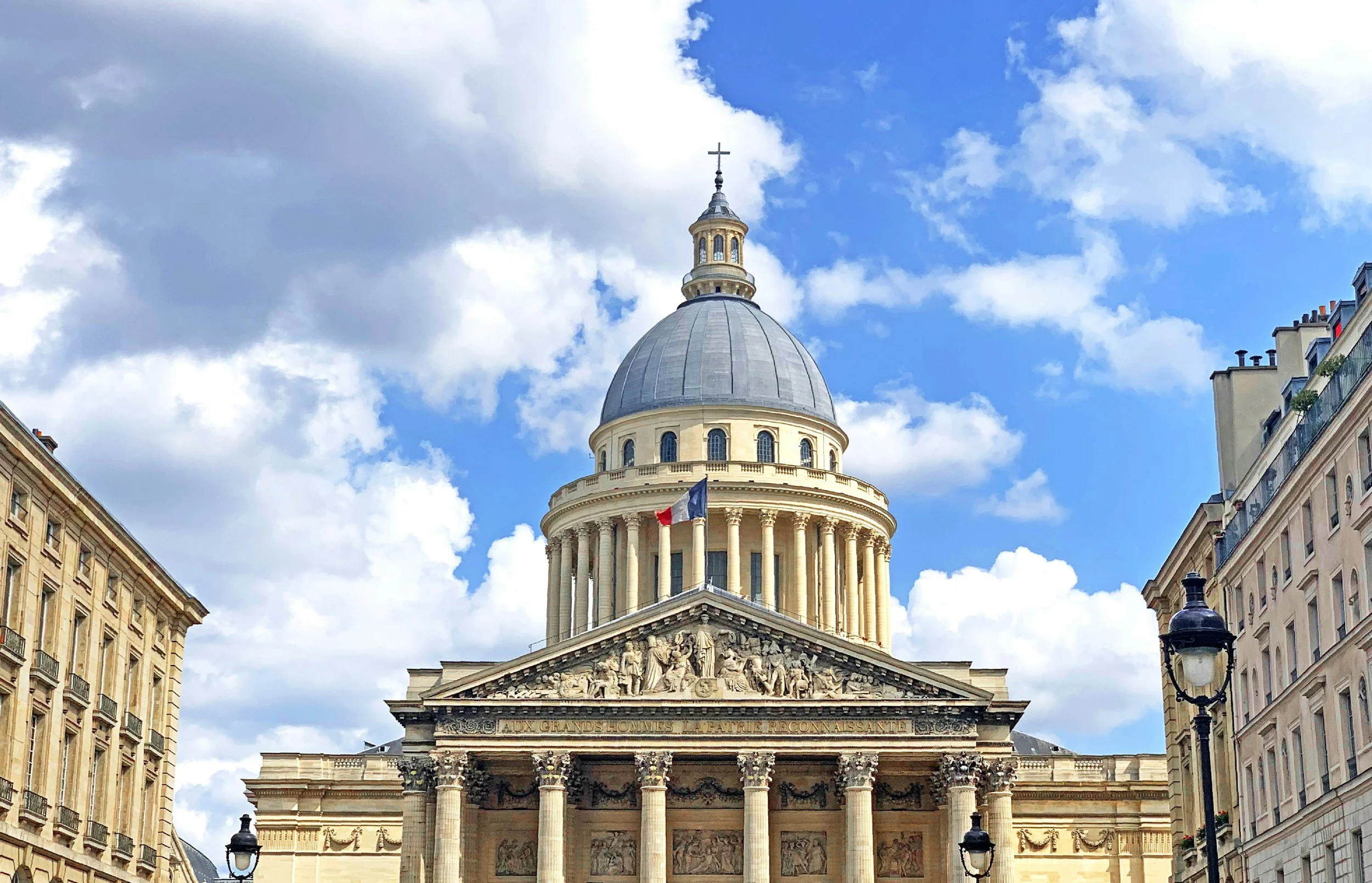 The Pantheon in Paris, France, with its domed roof and classical columns, under a partly cloudy sky.