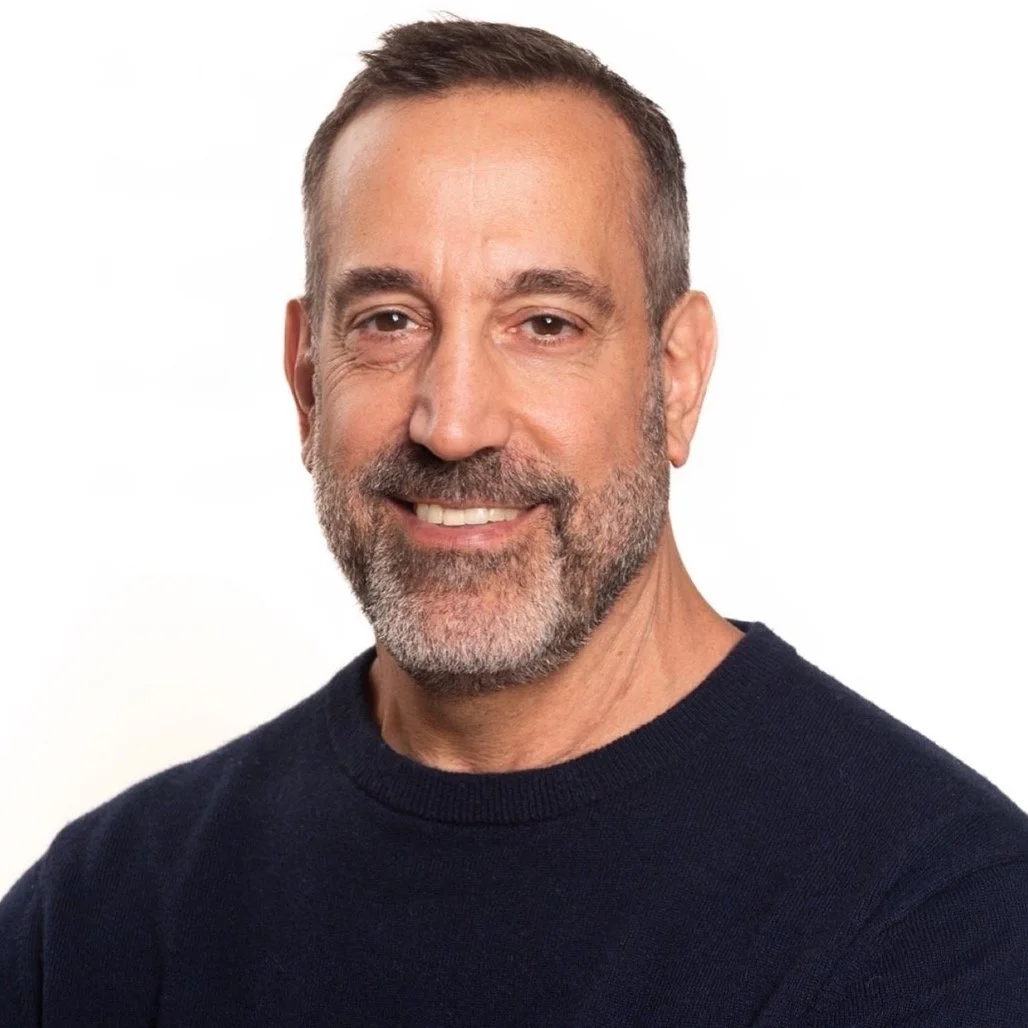 Smiling man with a beard wearing a dark sweater against a white background.