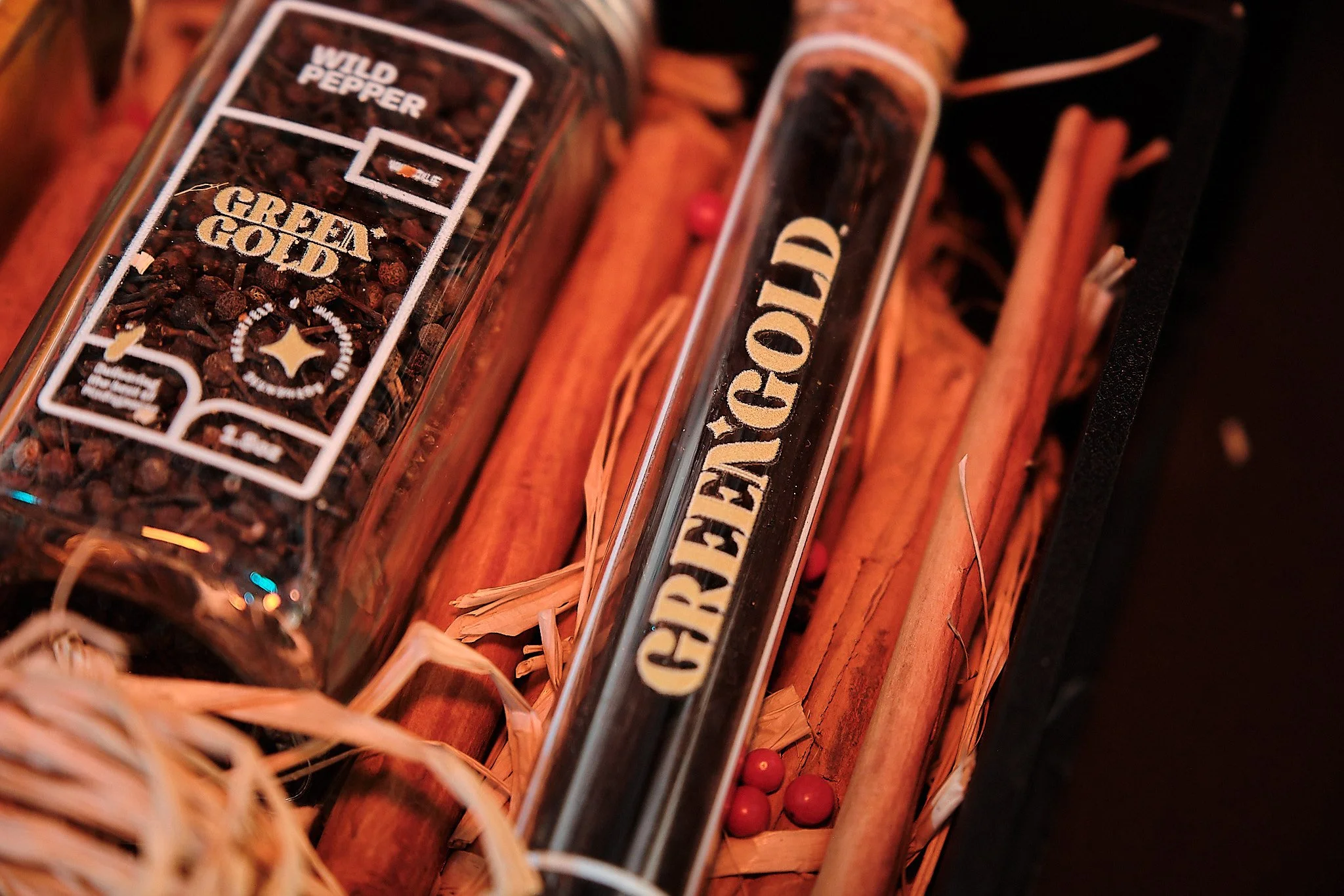 A close-up of a box containing cinnamon sticks, red berries, and two glass containers labeled 'Wild Reaper' and 'Grim Gold', with the labels indicating spices or flavorings.