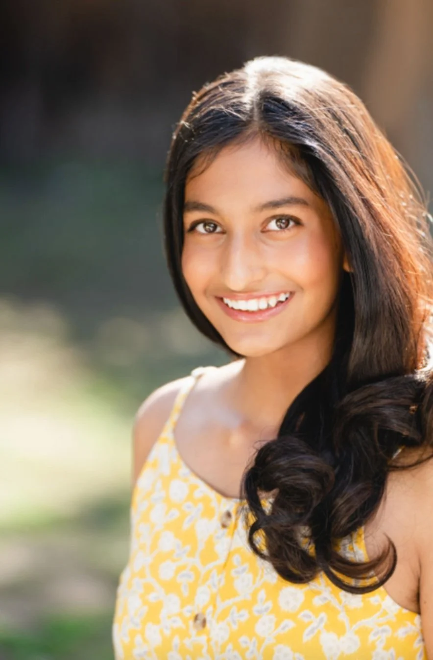 Zoya Founder of LoveYOU Project, with long dark hair wearing a yellow floral dress, outdoors.