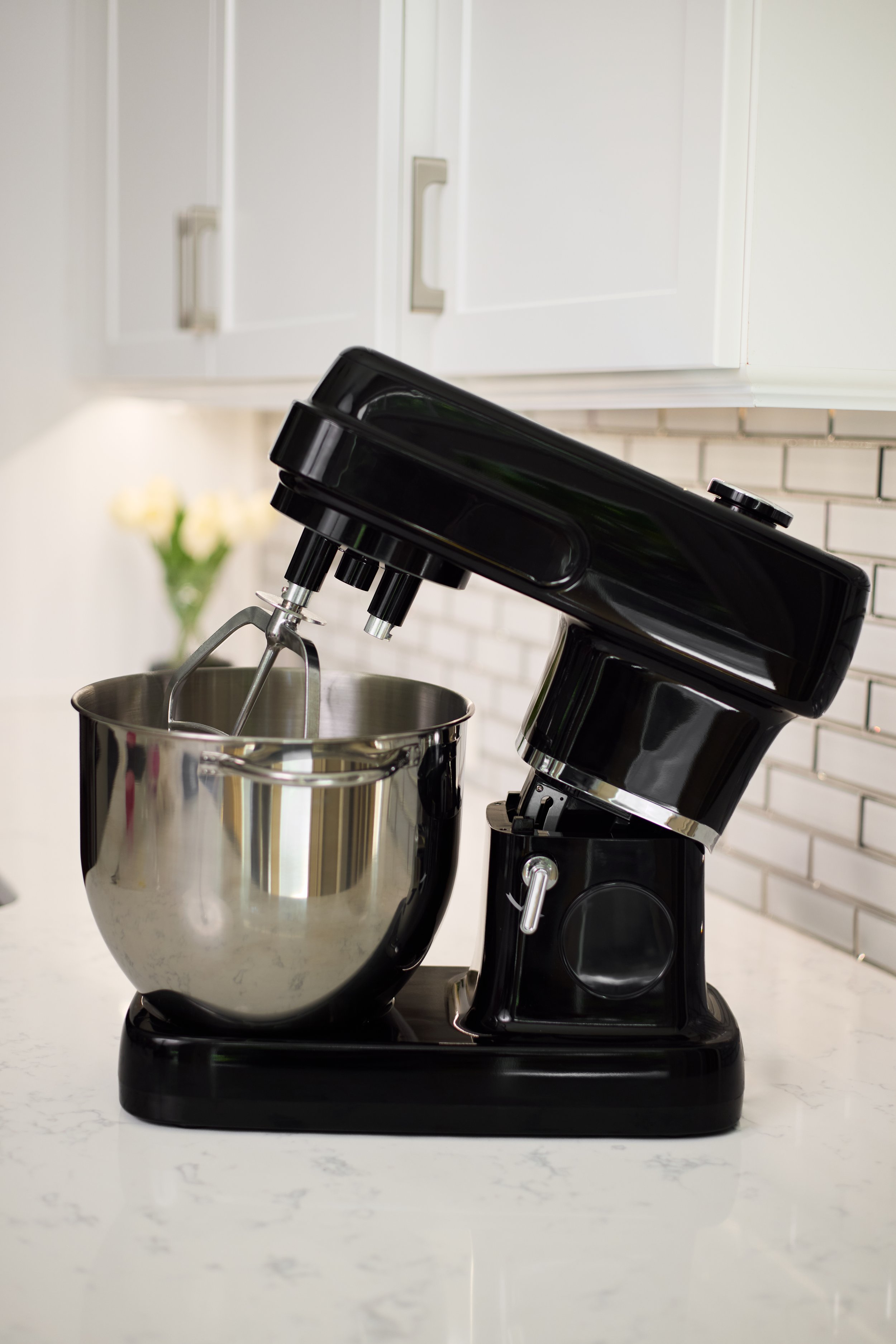 A black stand mixer with a stainless steel mixing bowl and a hand mixer attachment on a white kitchen countertop.