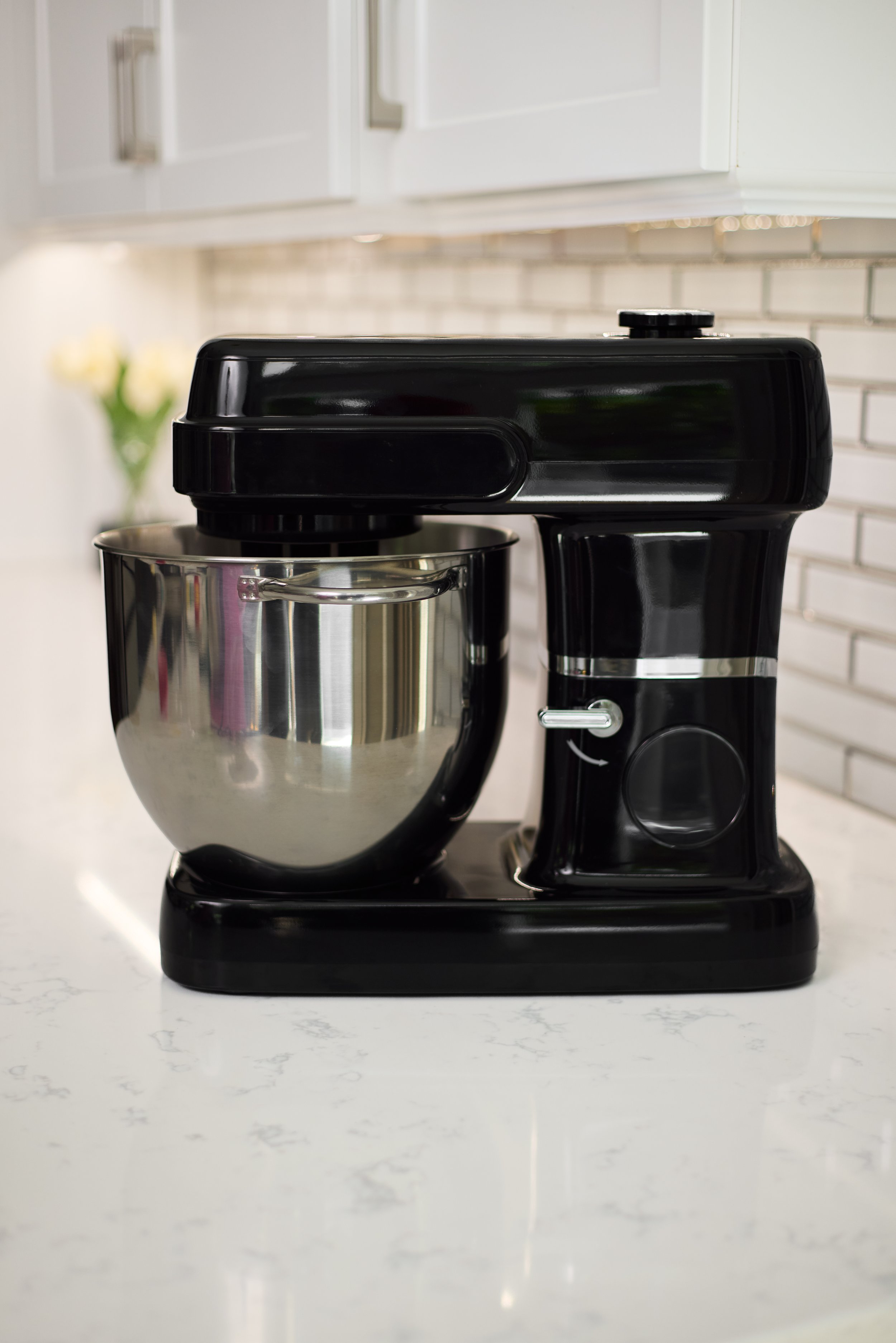 Black stand mixer with a metallic mixing bowl on a white kitchen countertop.