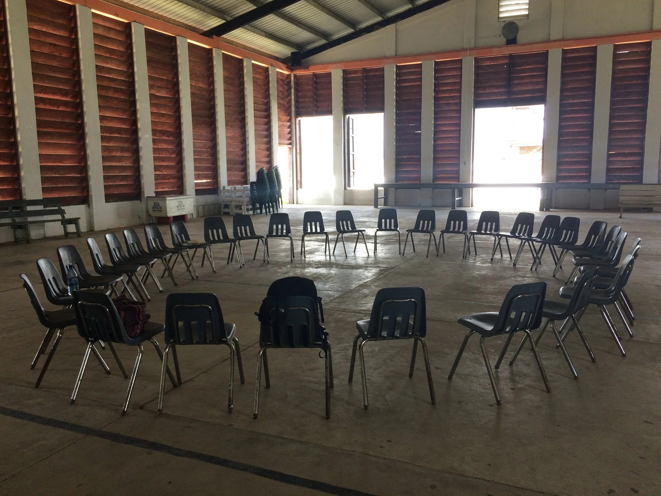 Young man sitting on a bench against a neutral wall, wearing a gray polo shirt and beige pants, with a contemplative expression and shadow cast on the wall.